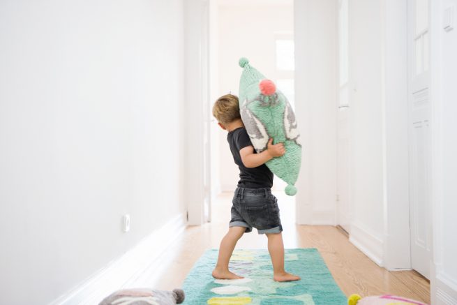 Junge spielt mit Kissen in einem hellen Altbauflur