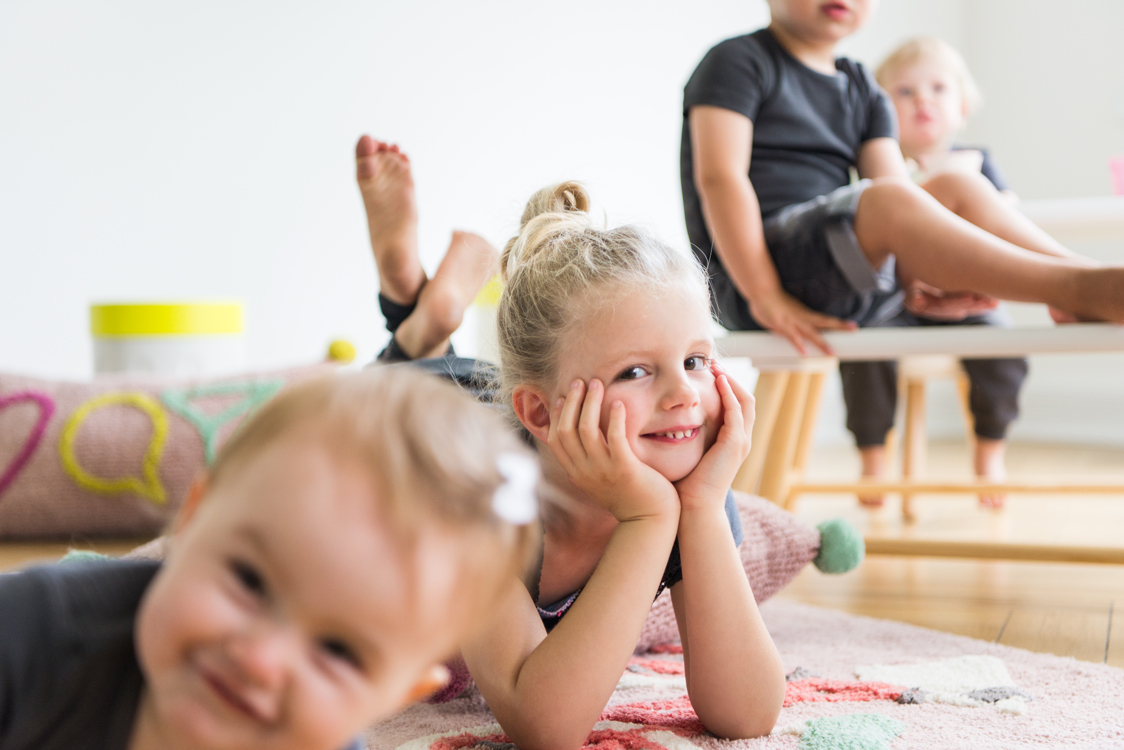 Blondes Mädchen lächelt in die Kamera und liegt auf einem Teppich in einer Altbauwohnung