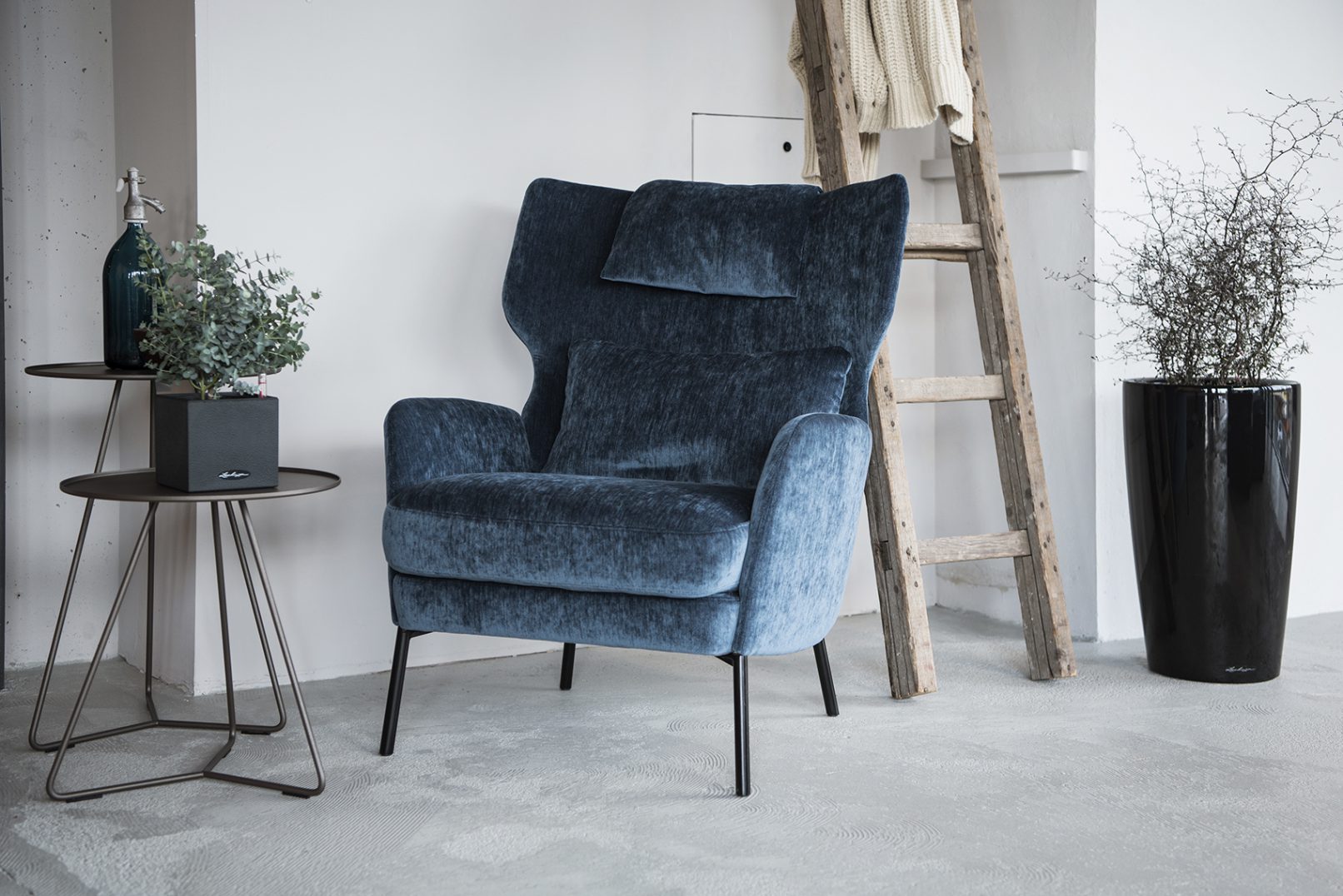 Interiorfotografie Hamburg im Scandi Look mit dunkelblauem Samt Sessel und grauem Beton mit Person