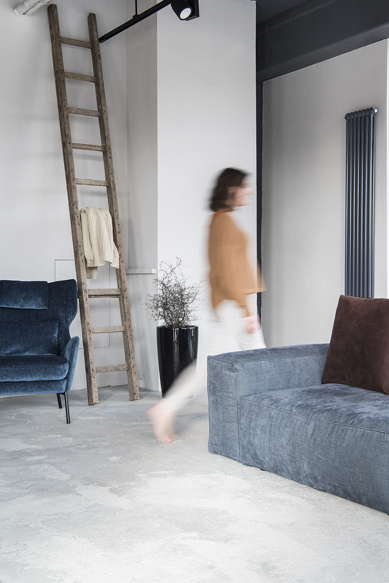 Interiorfotografie Hamburg im Scandi Look mit dunkelblauem Samt Sessel und grauem Beton mit Person in Bewegungsunschärfe