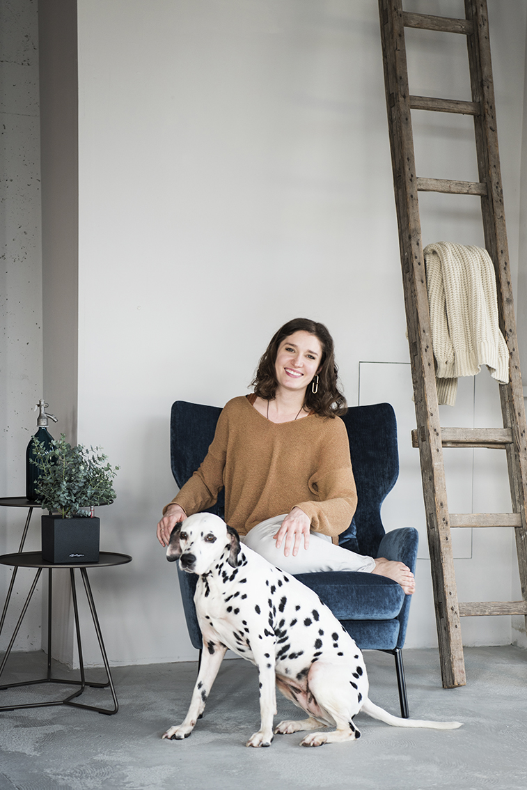 Interiorfotografie Hamburg im Scandi Look mit dunkelblauem Samt Sessel und grauem Beton mit Person