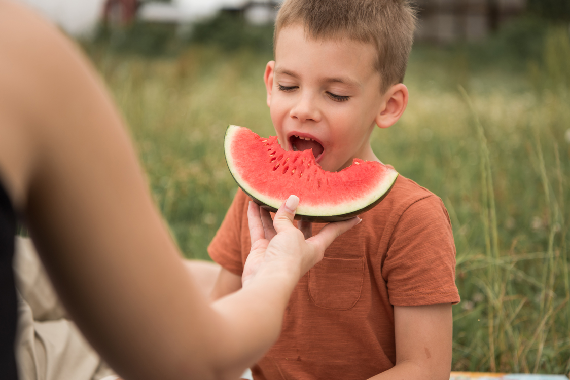 Kidsfotografie Lifestylefotografie in Hamburg Junge isst Wassermelone auf einer Sommerwiese