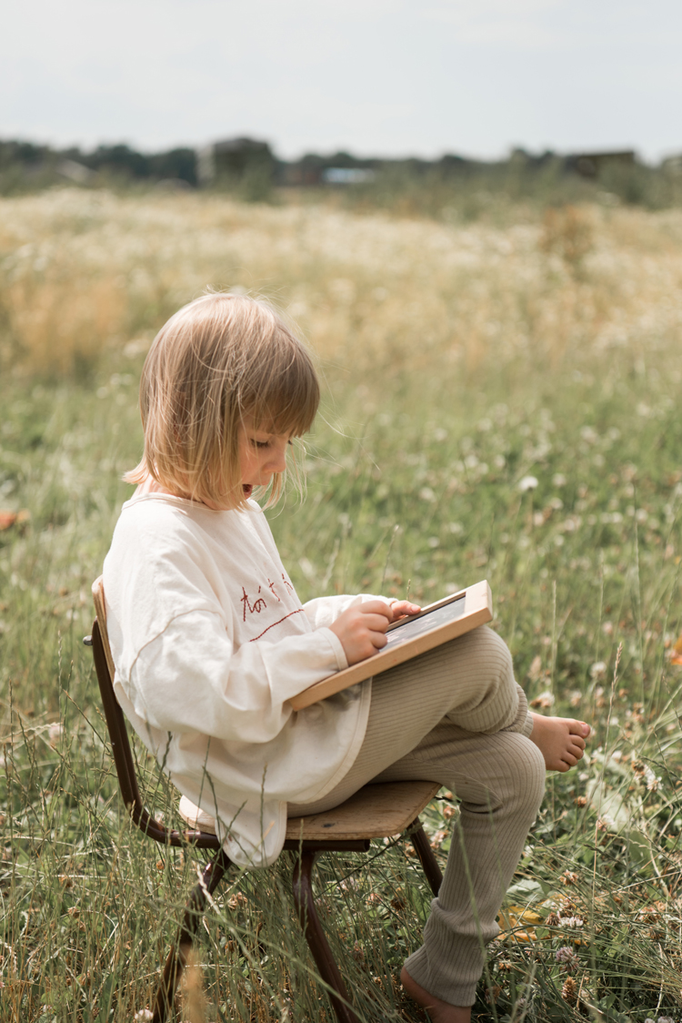Kidsfotografie Lifestylefotografie in Hamburg Mädchen sitzt auf einem Stuhl auf einer Sommerwiese und liest ein Buch
