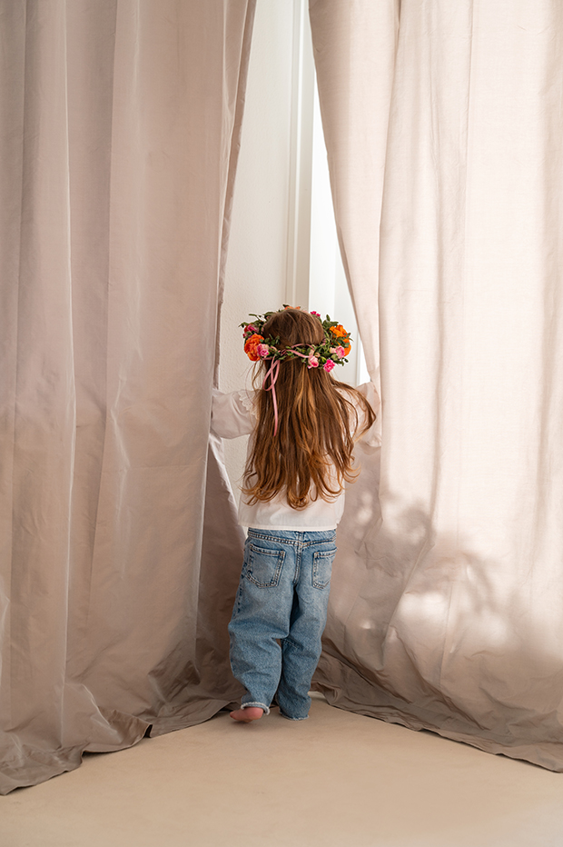 Kind in heller Kleidung tanzt barfuß mit Kuscheltier vor Stoffkulisse – natürliche People- und Lifestylefotografie mit sanftem Licht