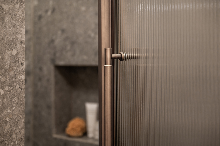 Detailaufnahme einer Glasdusche mit Edelstahlgriff und Natursteinwand im modernen Badezimmer in der HafenCity Hamburg