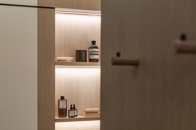 Beleuchtete Holzregale mit Pflegeprodukten und Handtüchern in modernem Badezimmer in der HafenCity Hamburg