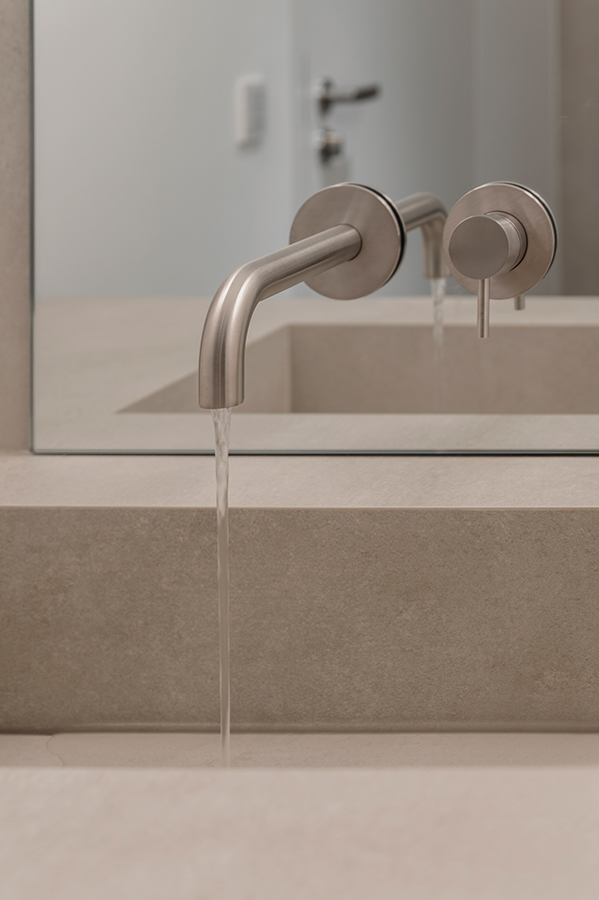 Detailaufnahme einer modernen Waschtischarmatur aus gebürstetem Edelstahl mit fließendem Wasser in einem Badezimmer in der HafenCity Hamburg