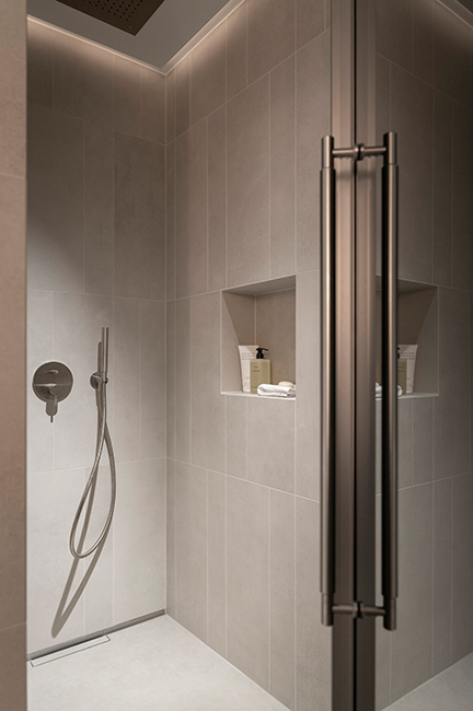 Moderne begehbare Dusche mit Glasfront, Natursteinwänden und Edelstahlarmatur in einem Badezimmer in der HafenCity Hamburg