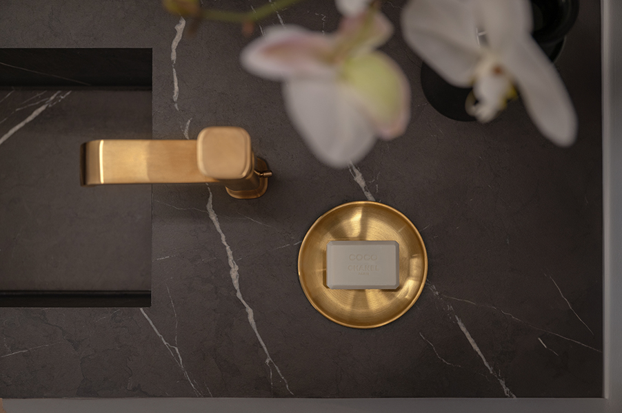 Goldene Armatur und Seifenschale auf dunkler Marmoroberfläche mit Orchidee, Interiorfotografie eines modernen Badezimmers in der Hamburger HafenCity.