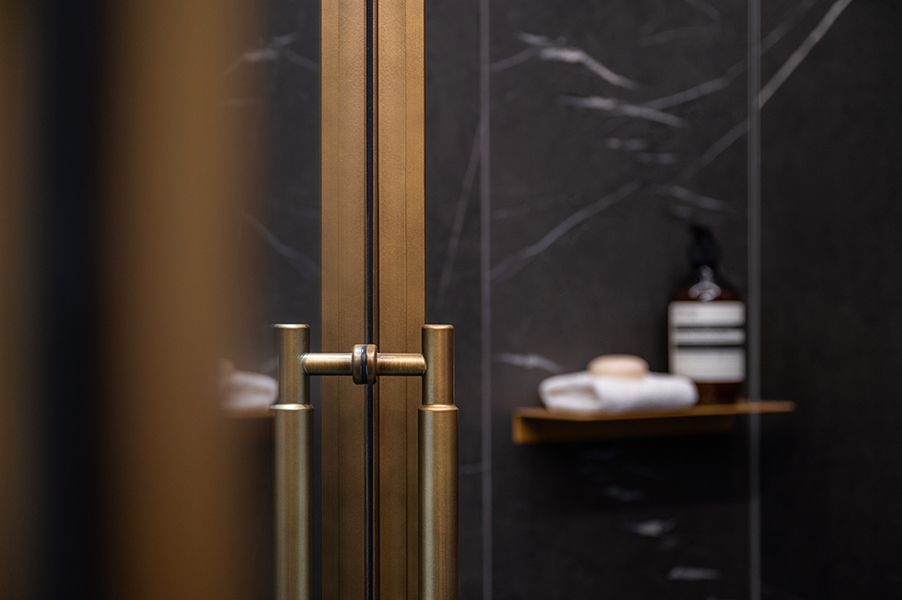 Duschbereich mit dunklen Marmorwänden, goldenen Armaturen und Ablage mit Pflegeprodukten, fotografiert in der Hamburger HafenCity.