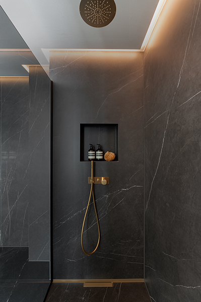 Dunkle Dusche mit Marmorwänden, goldener Armatur und integrierter Ablage, fotografiert in der Hamburger HafenCity.