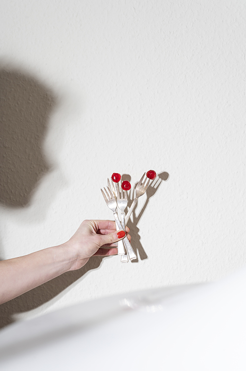 Hand hält mehrere Gabeln mit roten Beeren, reduziertes Food Stilllife in natürlichem Licht