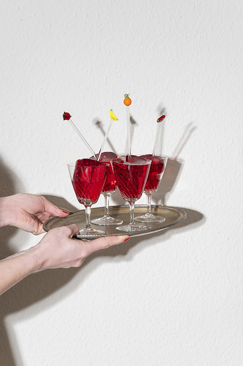 Tablett mit mehreren roten Drinks in Gläsern, gehalten von Händen, moderne Hospitality Fotografie