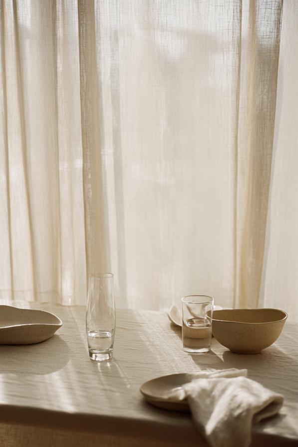 Keramikschalen auf Tisch mit weichem Licht und Vorhängen in minimalistischer Interior Szene