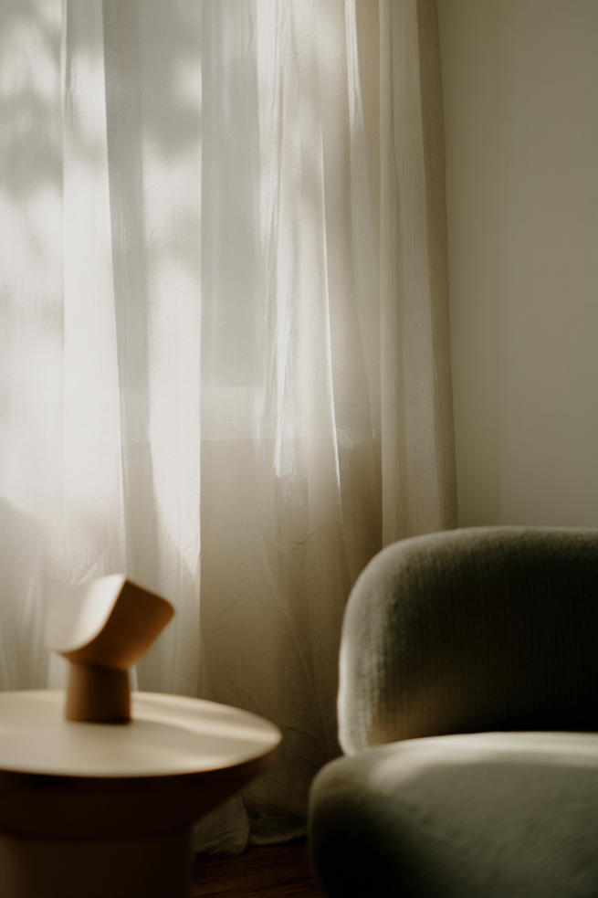 Warmes Interior Stillleben mit Keramikobjekt auf Beistelltisch neben Sessel und Vorhang im weichen Licht