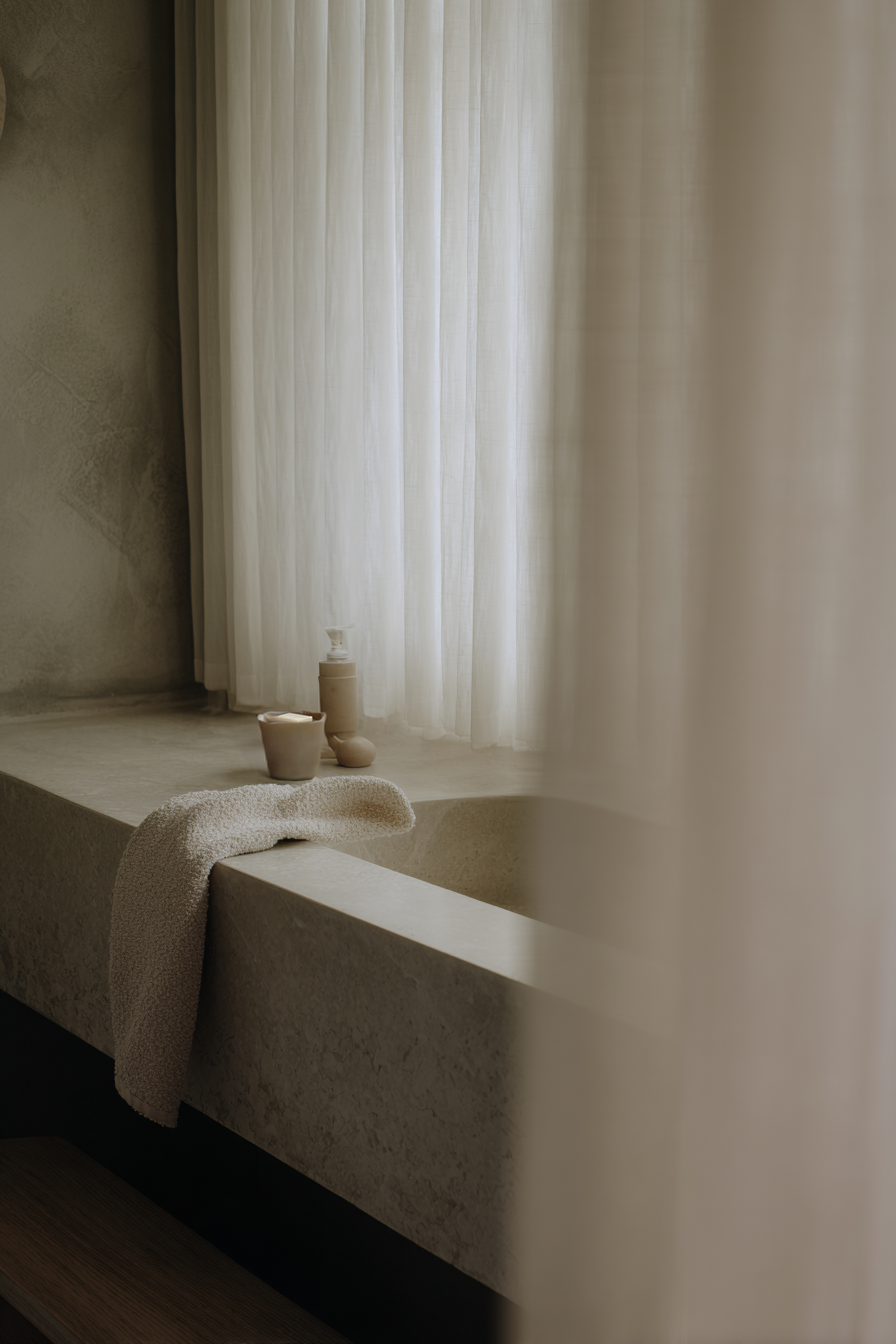 Minimalistisches Interior mit Keramikobjekten auf Bank vor Vorhang im warmen Fensterlicht