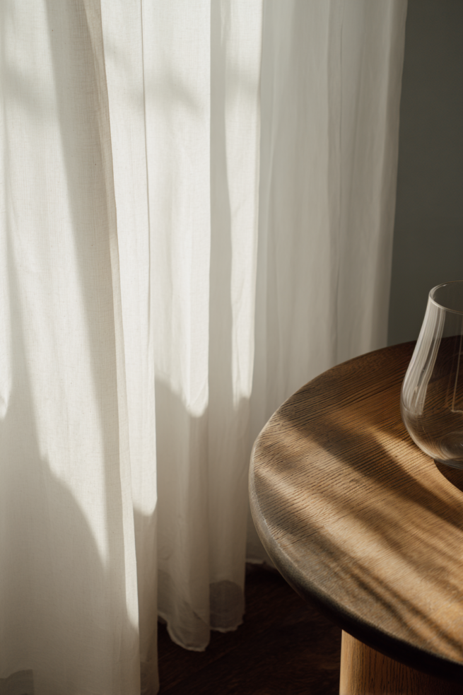 Licht und Schatten auf Vorhang neben Holztisch mit Keramikvase im warmen Tageslicht