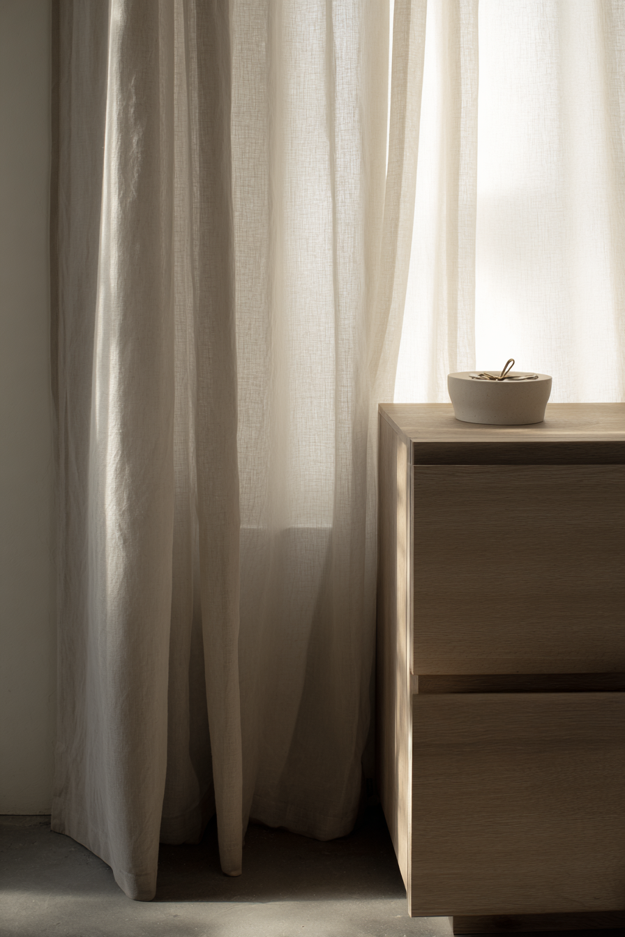 Holzkommode mit Keramikschale im warmen Tageslicht neben weichen Vorhängen