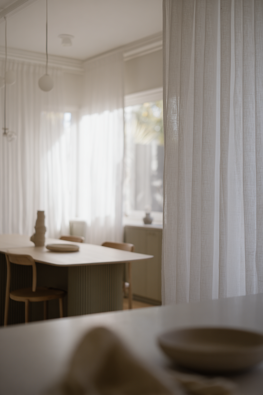 Essbereich mit Holztisch und Keramik im weichen Tageslicht vor Vorhängen