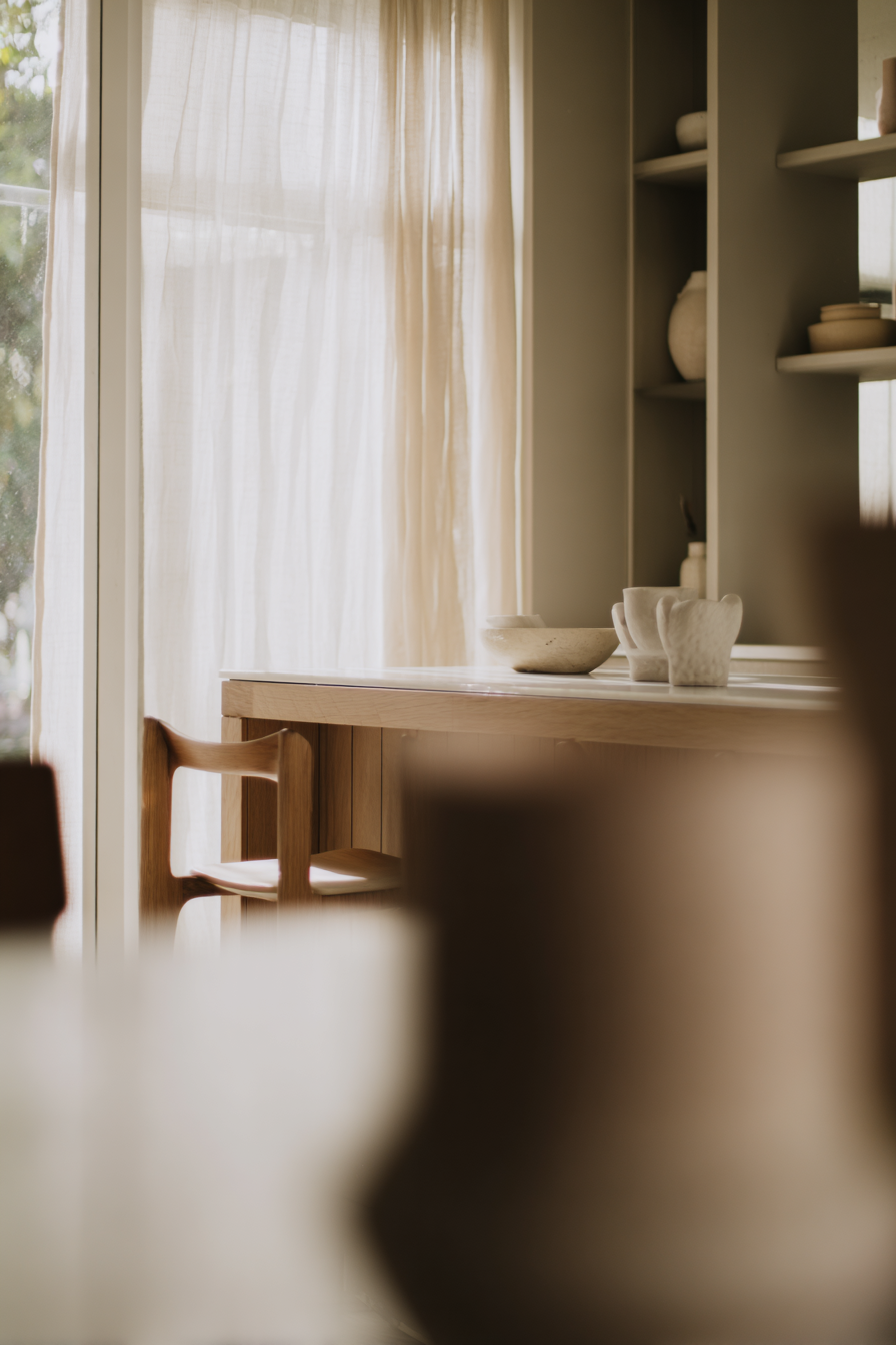 Skandinavisches Interior mit Holztisch, Keramikgeschirr und Regal im warmen Fensterlicht